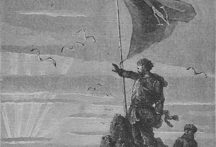 A man standing on a rocky precipice gestures grandly at the sunset while a dark flag emblazoned with an N blows in the wind next to him